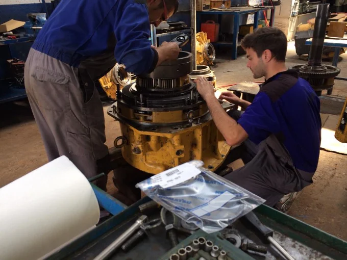 Dos mecánicos revisando el tren de rodaje y la transmisión de una máquina Komatsu en el taller